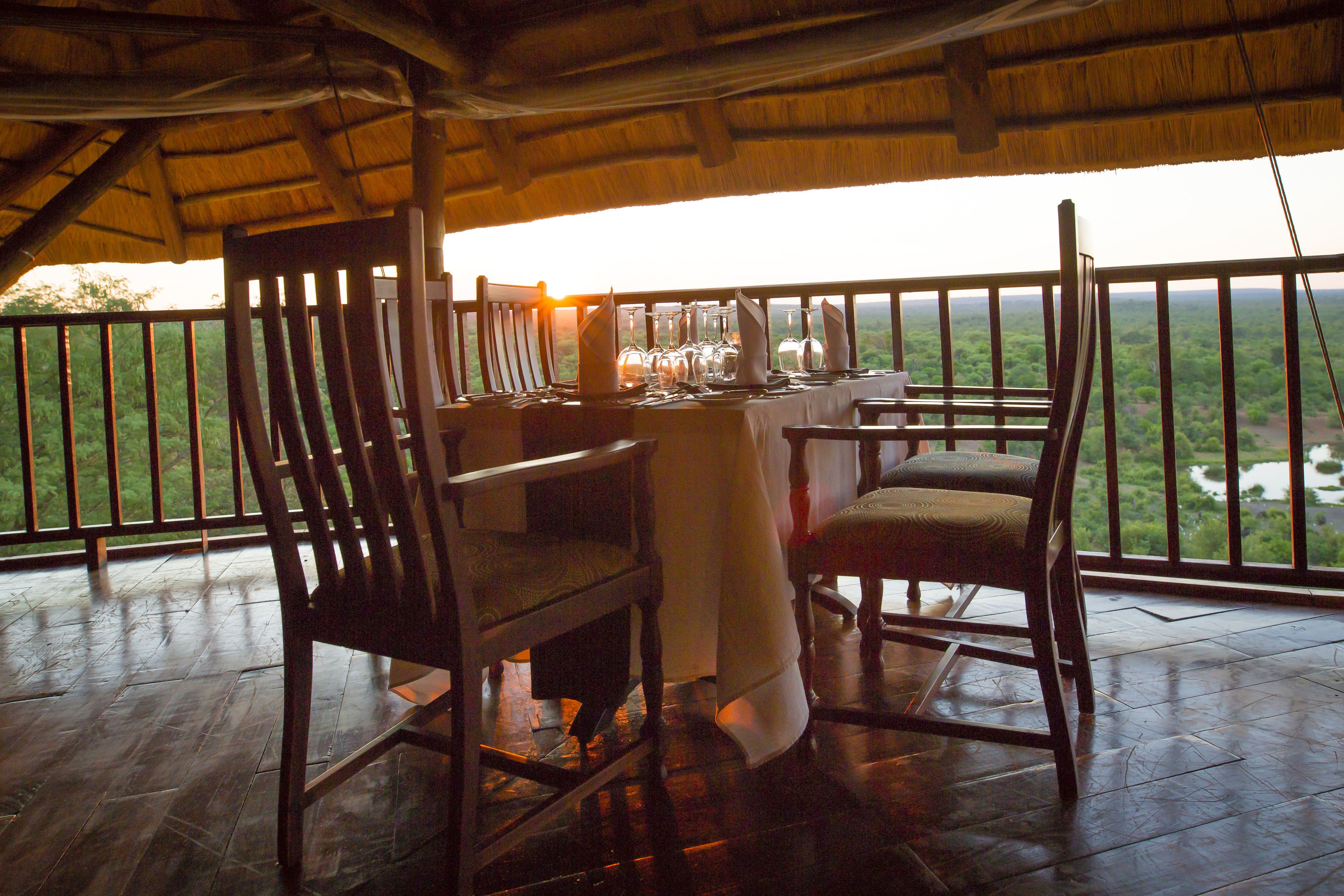 A wooden deck with a table set for dining, overlooking a lush landscape.
