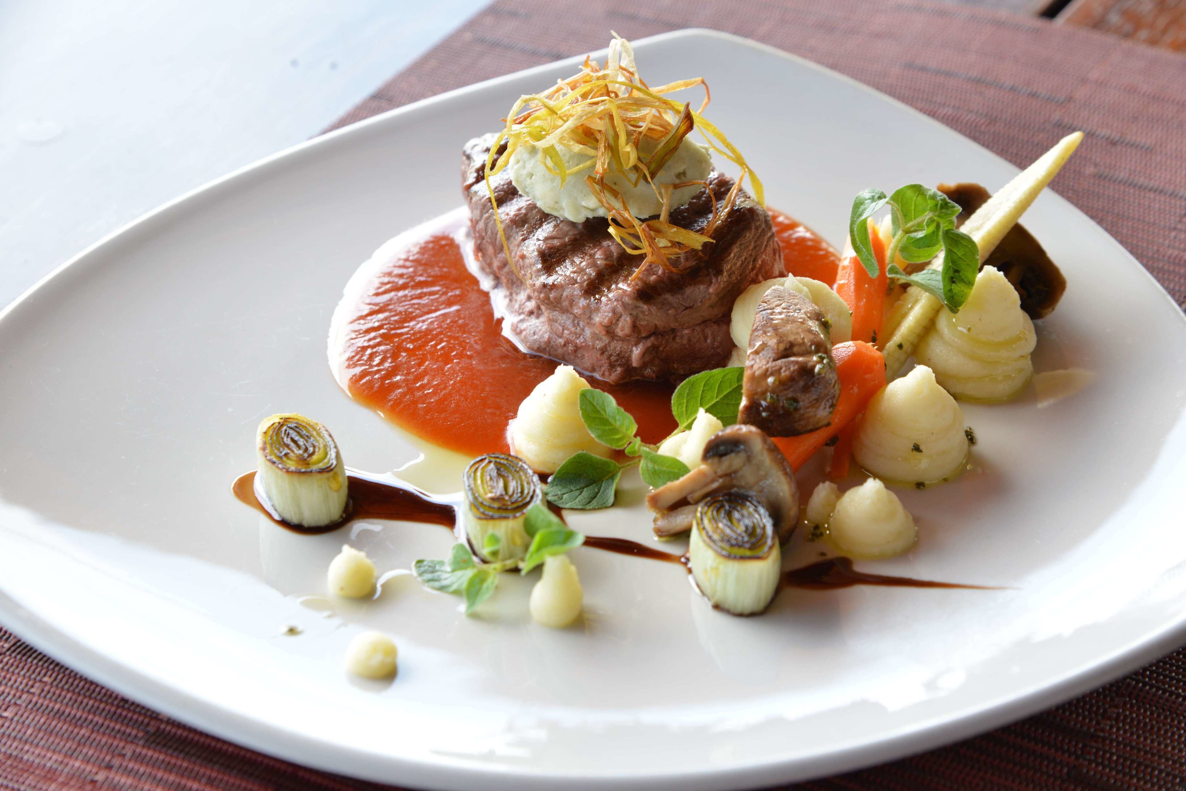 A white plate with a beef dish, vegetables, and sauce.