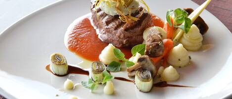 A white plate with a beef dish, vegetables, and sauce.