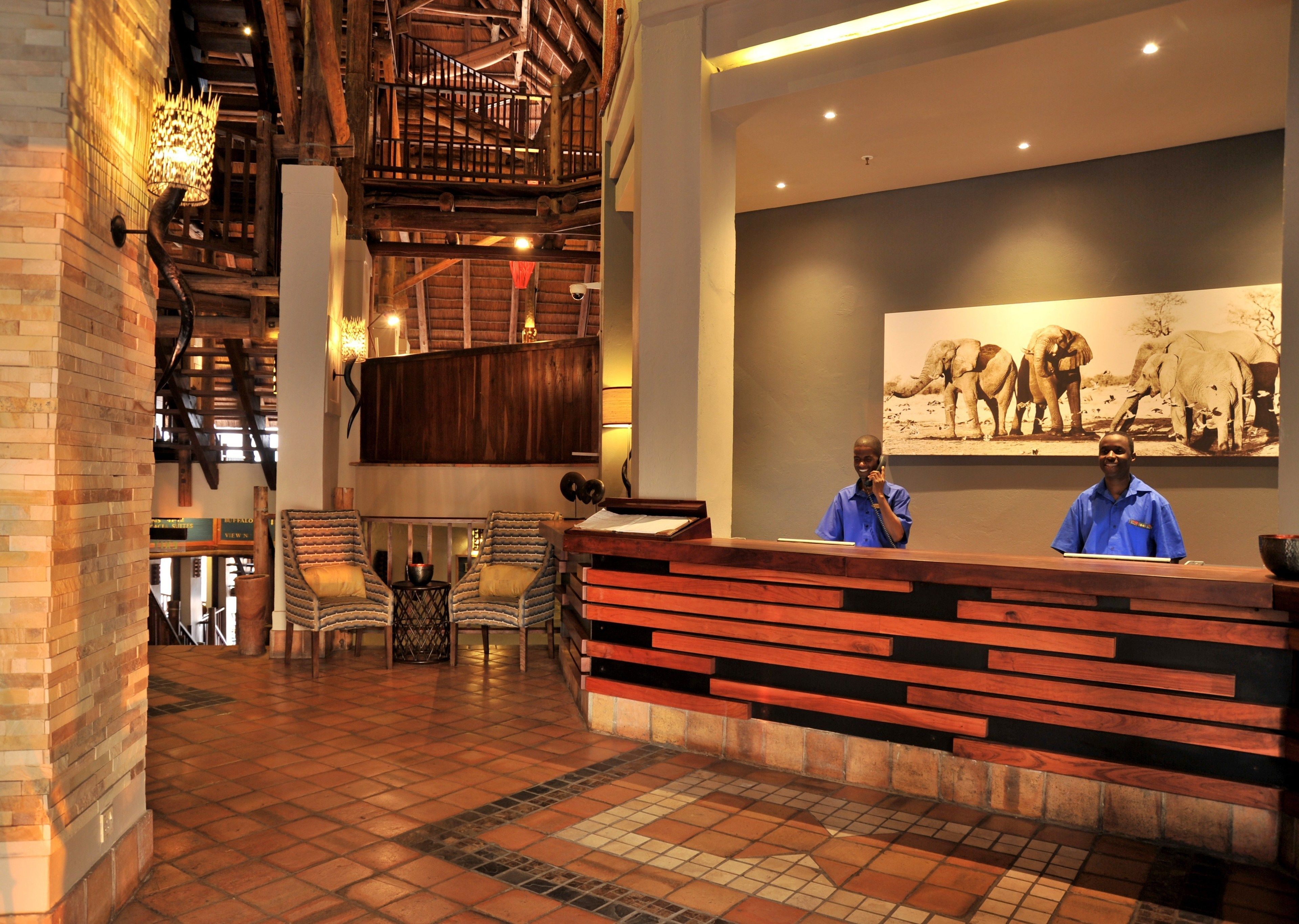 A reception area with a wooden reception desk, two chairs, a tiled floor, and a staircase with wooden railings.