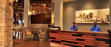 A reception area with a wooden reception desk, two chairs, a tiled floor, and a staircase with wooden railings.