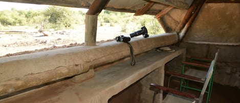 A rustic wooden bench with a camera on it, a green metal chair, and a view of the outdoors.