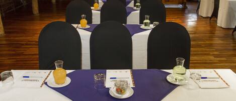 Un salón de conferencias con mesas dispuestas para una reunión, cada una con placas de identificación, botellas de agua y un pequeño recipiente de vidrio.