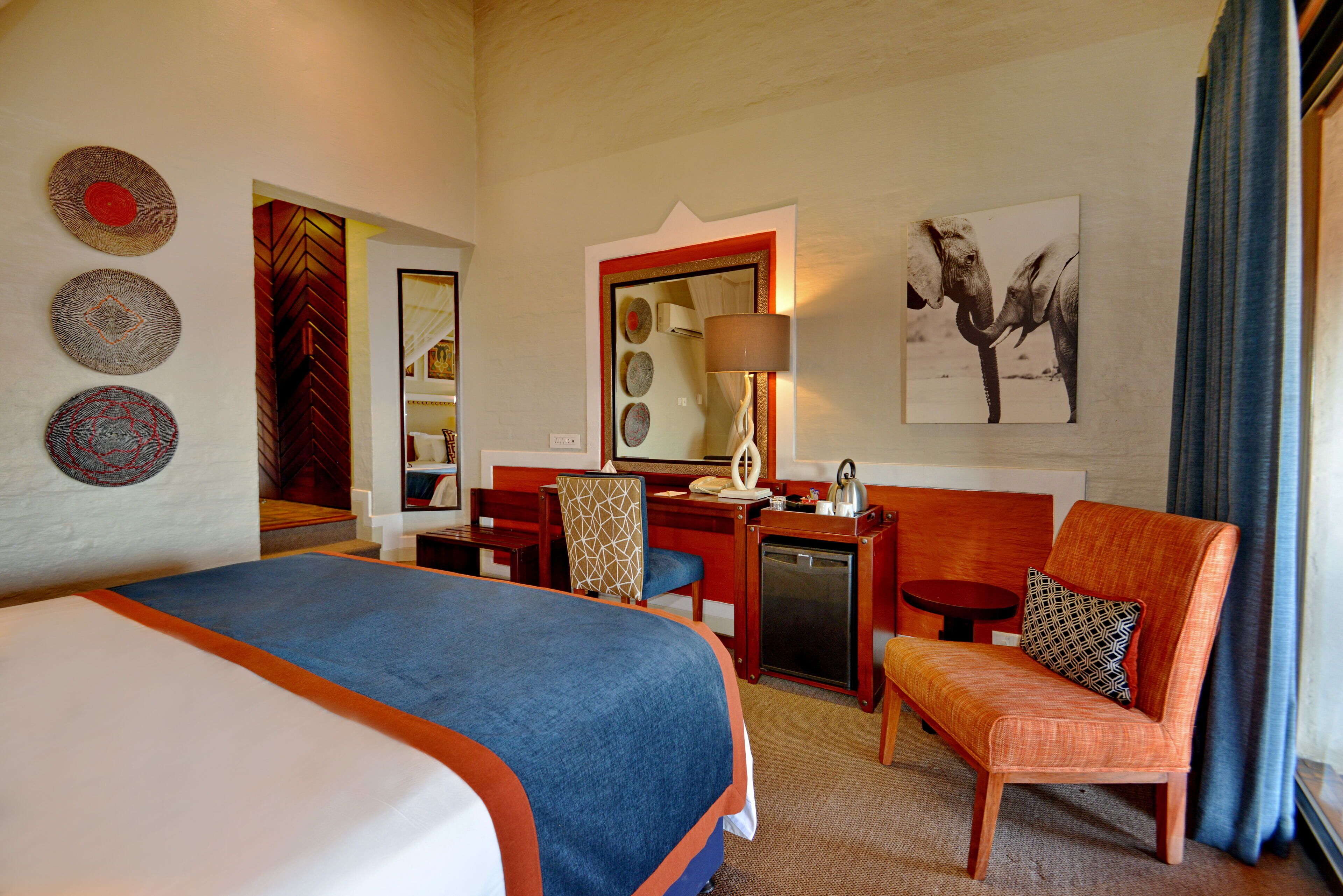 A hotel room with a bed, a desk, a chair, and a small table. There are wall decorations and a window with curtains.