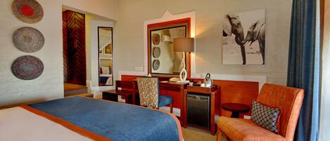A hotel room with a bed, a desk, a chair, and a small table. There are wall decorations and a window with curtains.