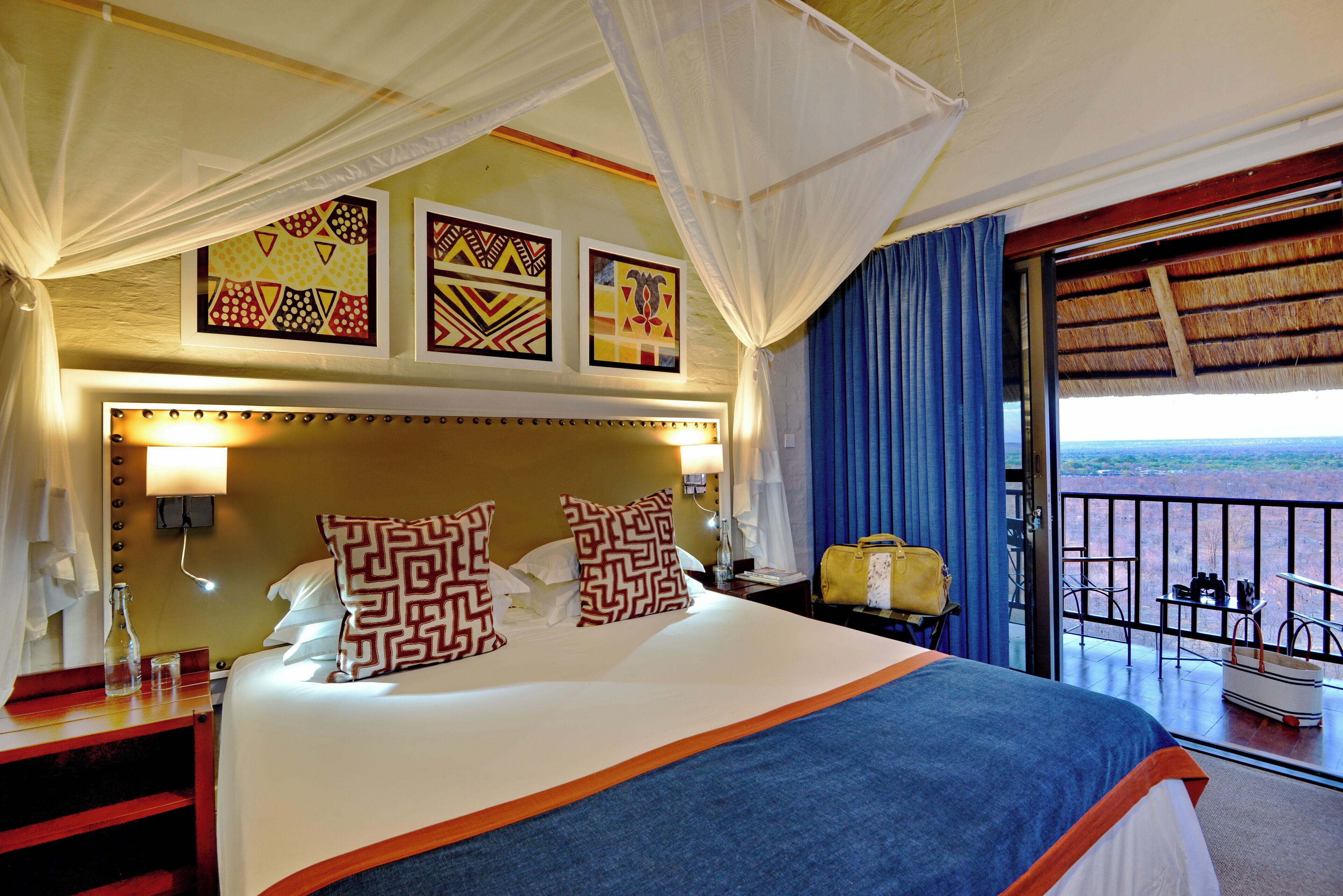 A hotel room with a bed, a nightstand, a lamp, a suitcase, and a balcony with a view.