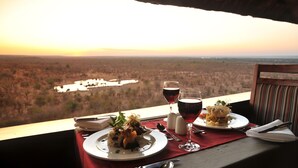 A table with a meal and wine glasses, overlooking a scenic landscape.