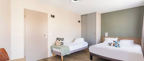 Una habitación de hotel moderna con dos camas, piso de madera, una lámpara en el techo y una puerta.