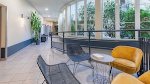 A modern indoor area with a curved balcony, black and yellow chairs, a small table, and large windows offering a view of greenery outside. - Appart'City Confort Niort Centre (Niort)