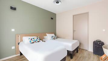 Ein Hotelzimmer mit zwei Einzelbetten, einem Holzkopfteil, einem Deckenventilator und einem Koffer auf dem Boden.