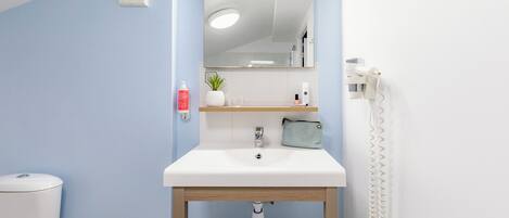 Un baño con lavamanos blanco, un espejo, toallero, inodoro y ducha.