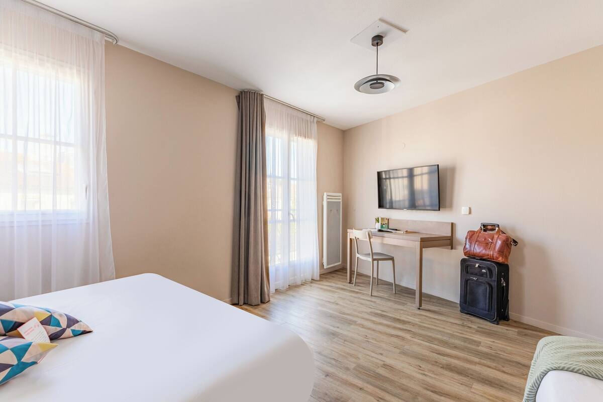 A hotel room with a bed, desk, chair, and a suitcase.