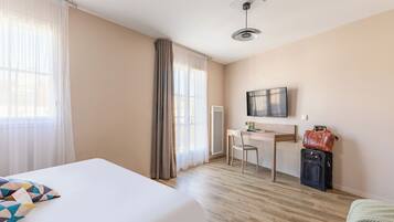 A hotel room with a bed, desk, chair, and a suitcase.