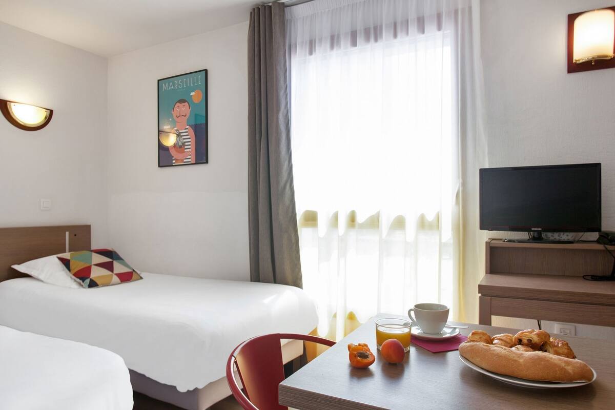Ein Hotelzimmer mit Bett, Fernseher, einem Esstisch mit Frühstück und einem Poster an der Wand.
