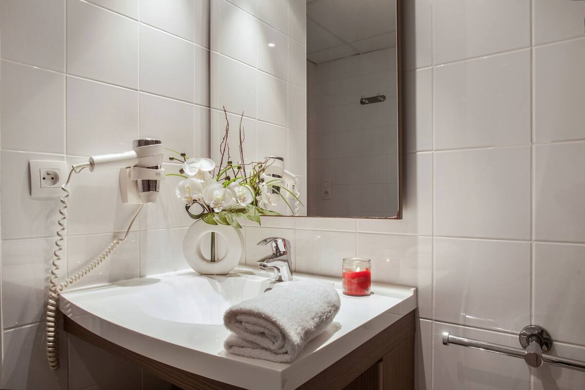 Ein Badezimmer mit weißem Waschbecken, einem Spiegel, einem Handtuch, einer Vase mit Blumen und einer Kerze.