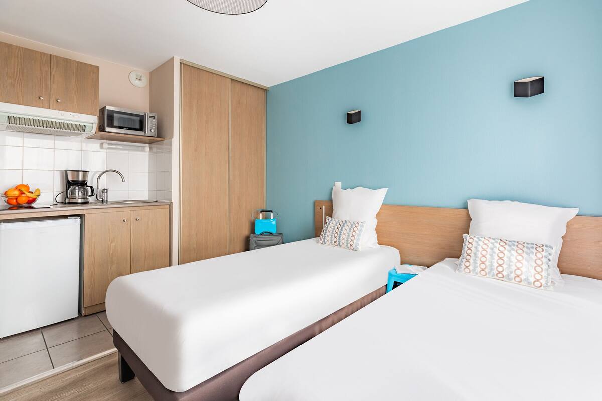 Ein Hotelzimmer mit zwei Betten, einer Küchenzeile und einer blauen Akzentwand.