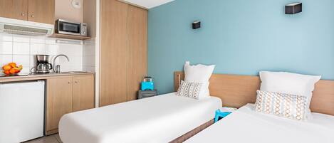 Habitación de hotel con dos camas, kitchenette y una pared azul de acento.
