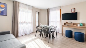 A modern living room with a sofa, dining table, chairs, and a TV mounted on the wall. - Appart'City Classic Marseille Euromed (Marseille)