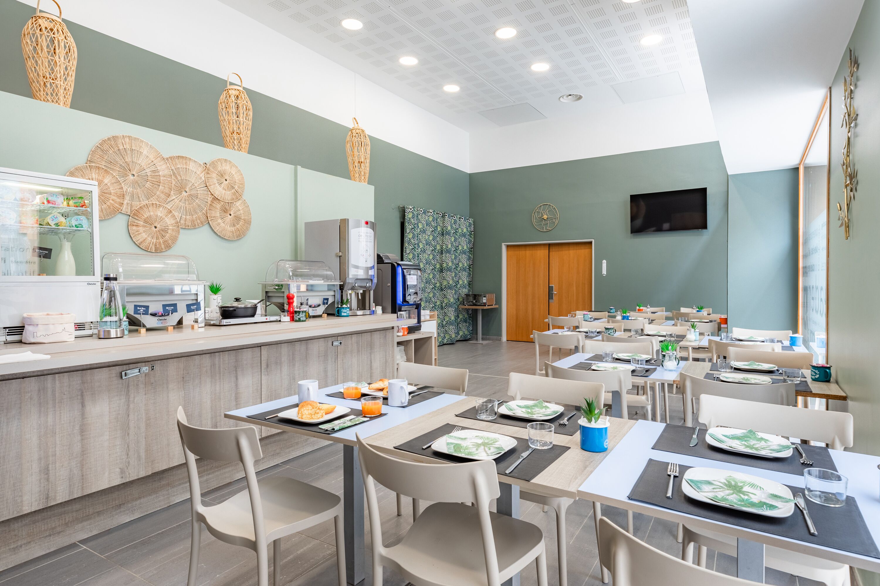A spacious dining area with multiple tables and chairs, a counter with food items, and a wall-mounted television.