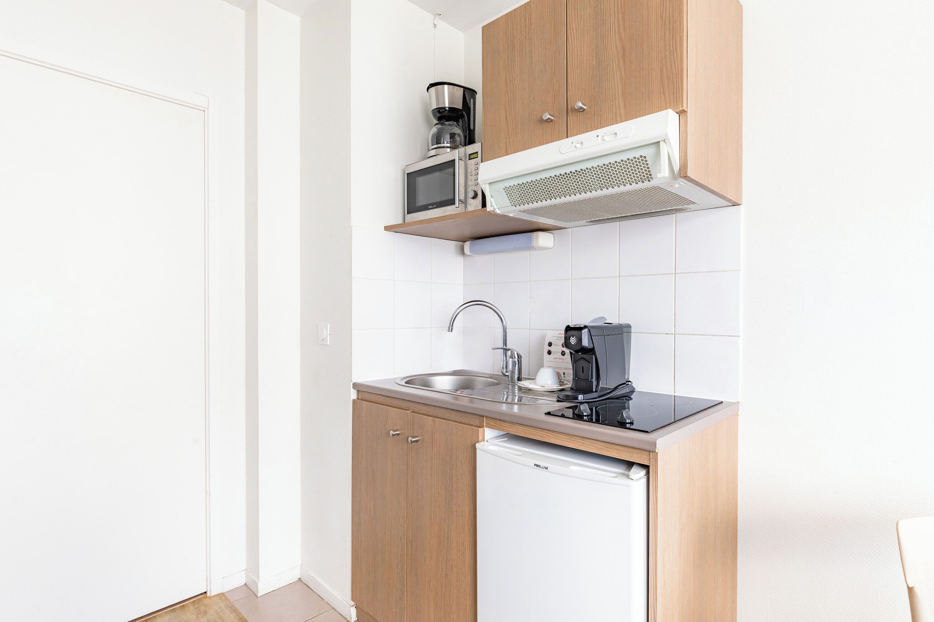A compact kitchen with wooden cabinets, a built-in microwave, a coffee maker, and a dishwasher.