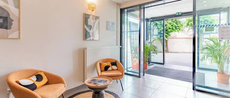 A modern reception area with two armchairs, a round table, and a glass door leading outside.
