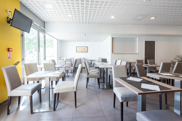 A modern conference room with white tables and chairs, a flat-screen TV mounted on the wall, and a large window providing natural light. - Zenitude Hôtel - Résidences Narbonne Centre (Narbonne)