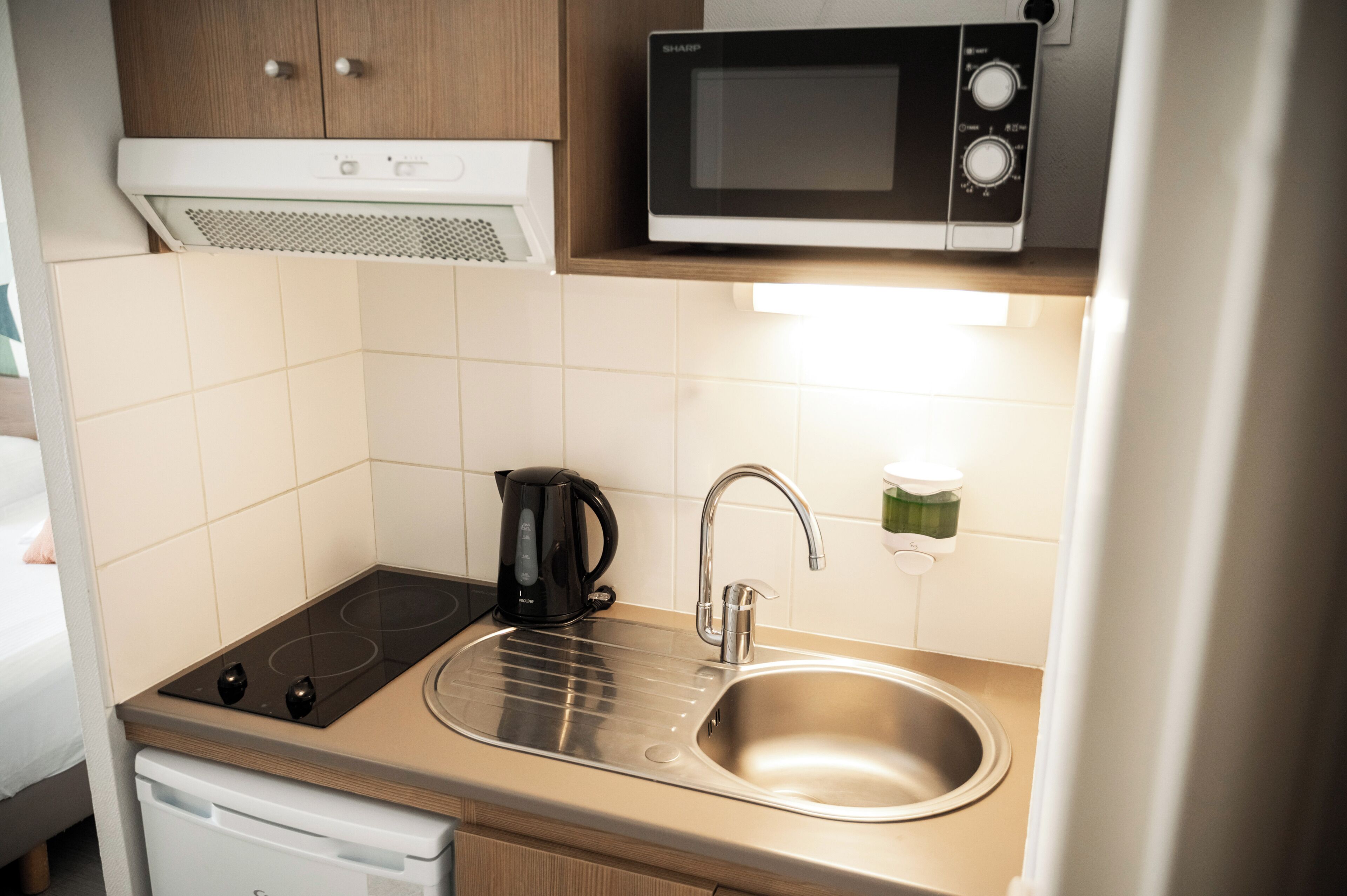 A compact kitchenette with a microwave, kettle, and stainless steel sink.