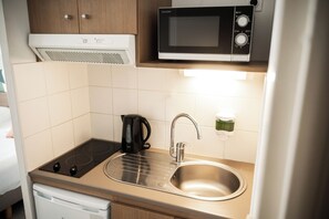 A compact kitchenette with a microwave, kettle, and stainless steel sink. - Zenitude Hôtel - Résidences Narbonne Centre (Narbonne)