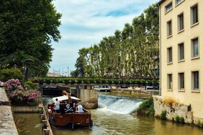 A boat on a river with a waterfall, surrounded by greenery and a bridge. - Zenitude Hôtel - Résidences Narbonne Centre (Narbonne)