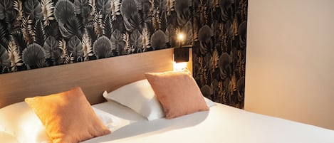 A neatly made bed with white linens and two brown pillows, set against a wall with a leaf-patterned wallpaper.