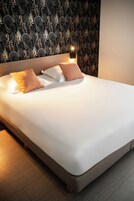 Una cama bien hecha con sábanas blancas y dos almohadas marrones, frente a una pared con papel tapiz estampado con hojas.