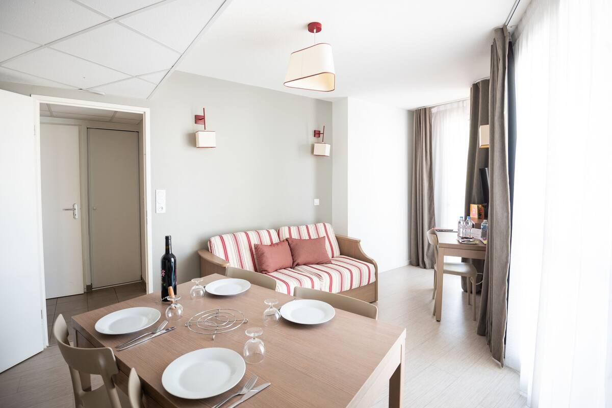 A dining area with a table set for four, a sofa, and a TV in the background.