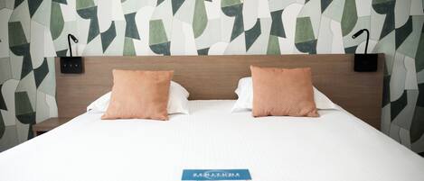 Habitación de hotel con cama, dos almohadas, una mesita de noche y una pared con diseño geométrico.