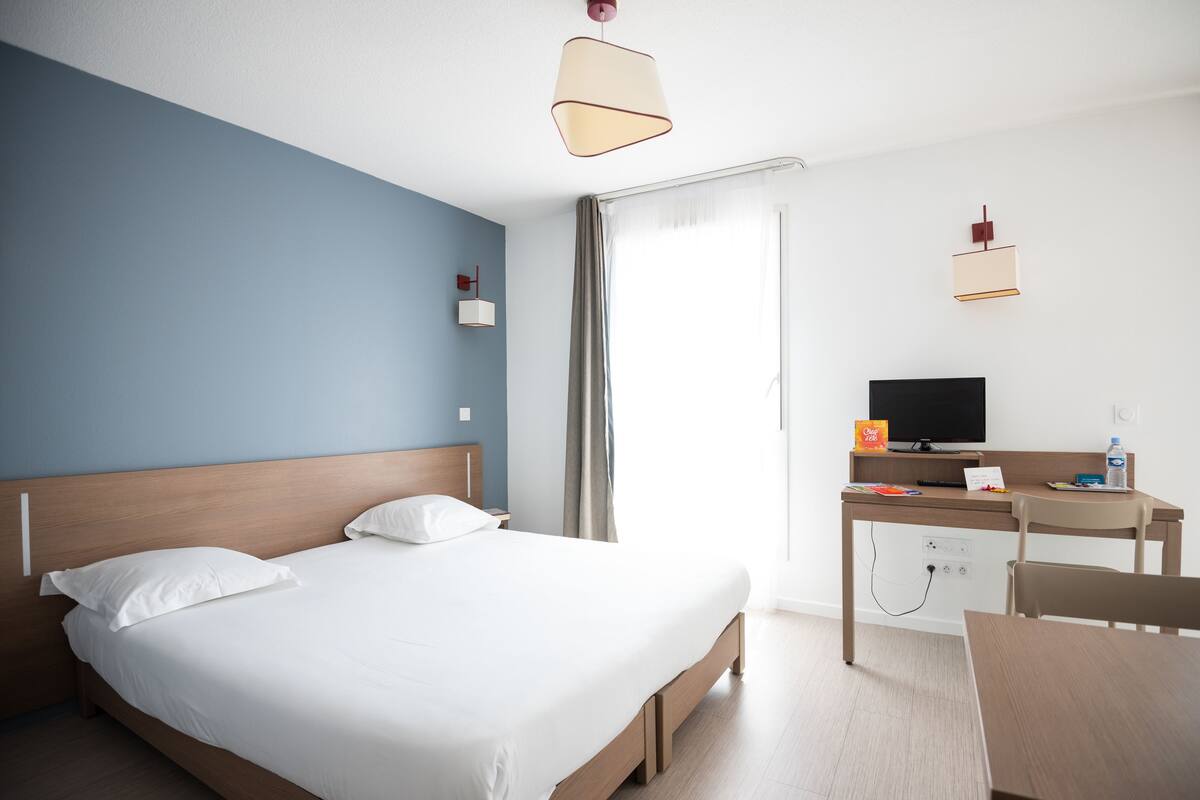 A hotel room with a bed, a desk, a chair, a television, and a window with curtains.