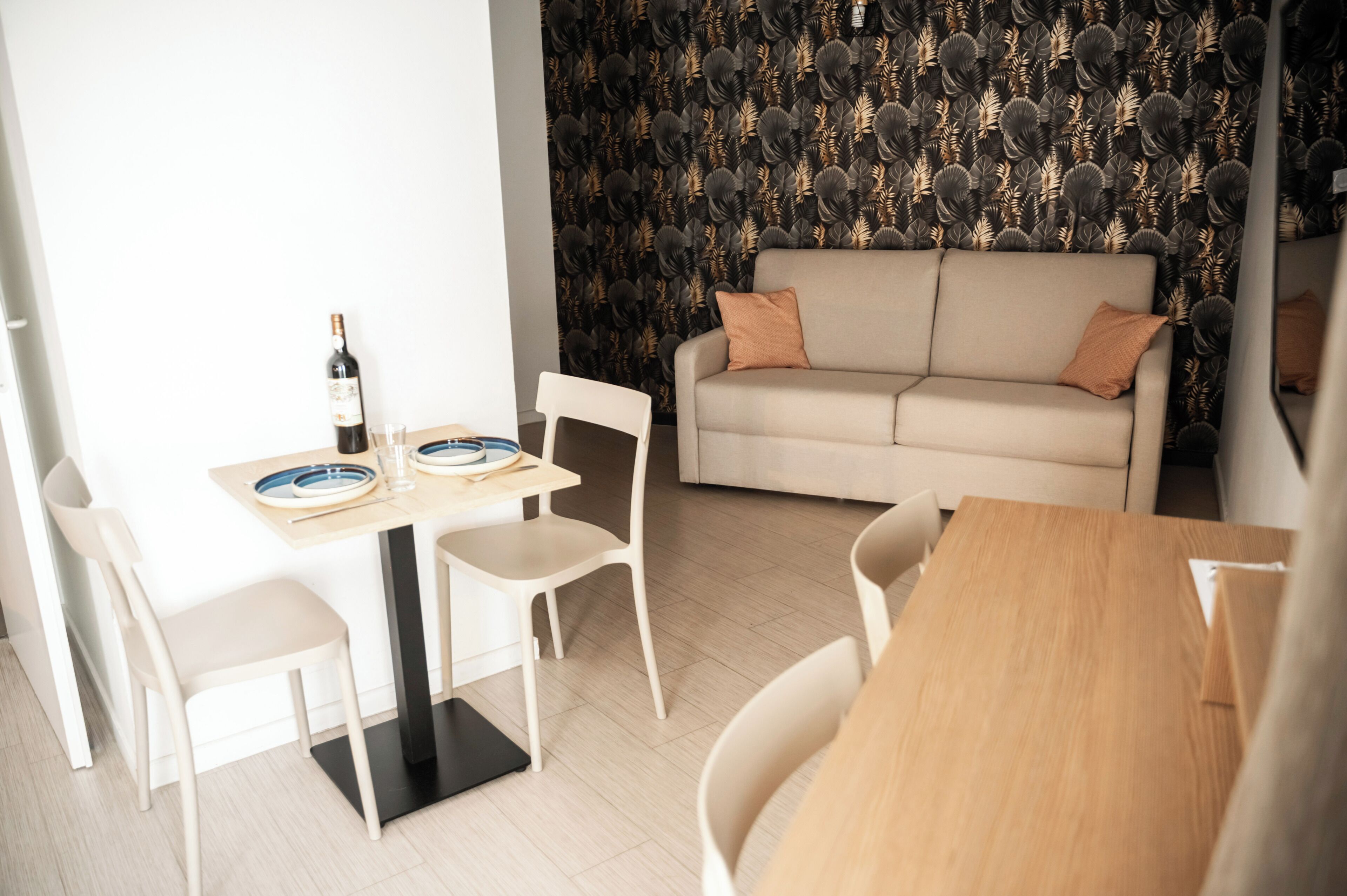 A modern living space with a dining area, a sofa, and a patterned wallpaper.