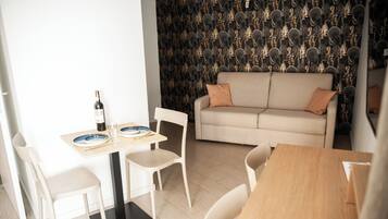 A modern living space with a dining area, a sofa, and a patterned wallpaper.