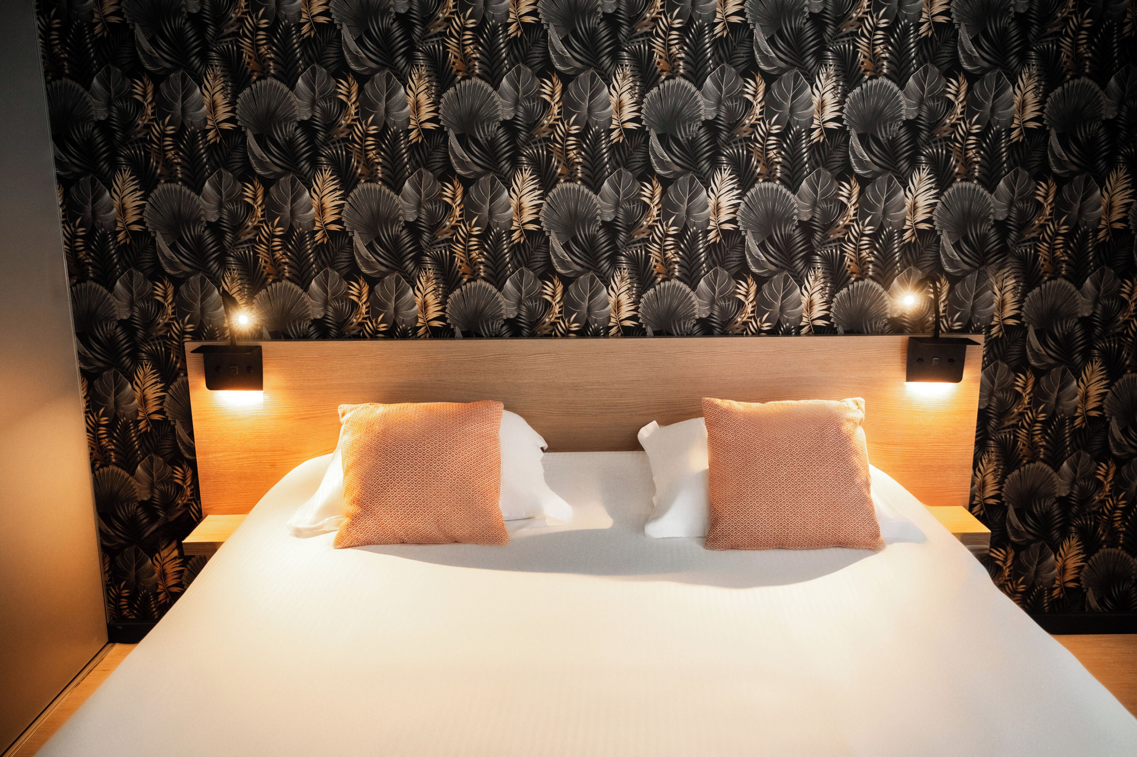 A hotel room with a large bed, two bedside lamps, and a wall with a leaf pattern.