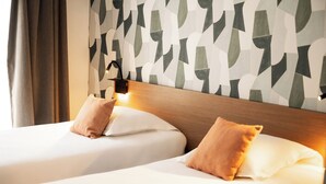 Habitación de hotel con dos camas, cabecera de madera y pared con estampado geométrico.
