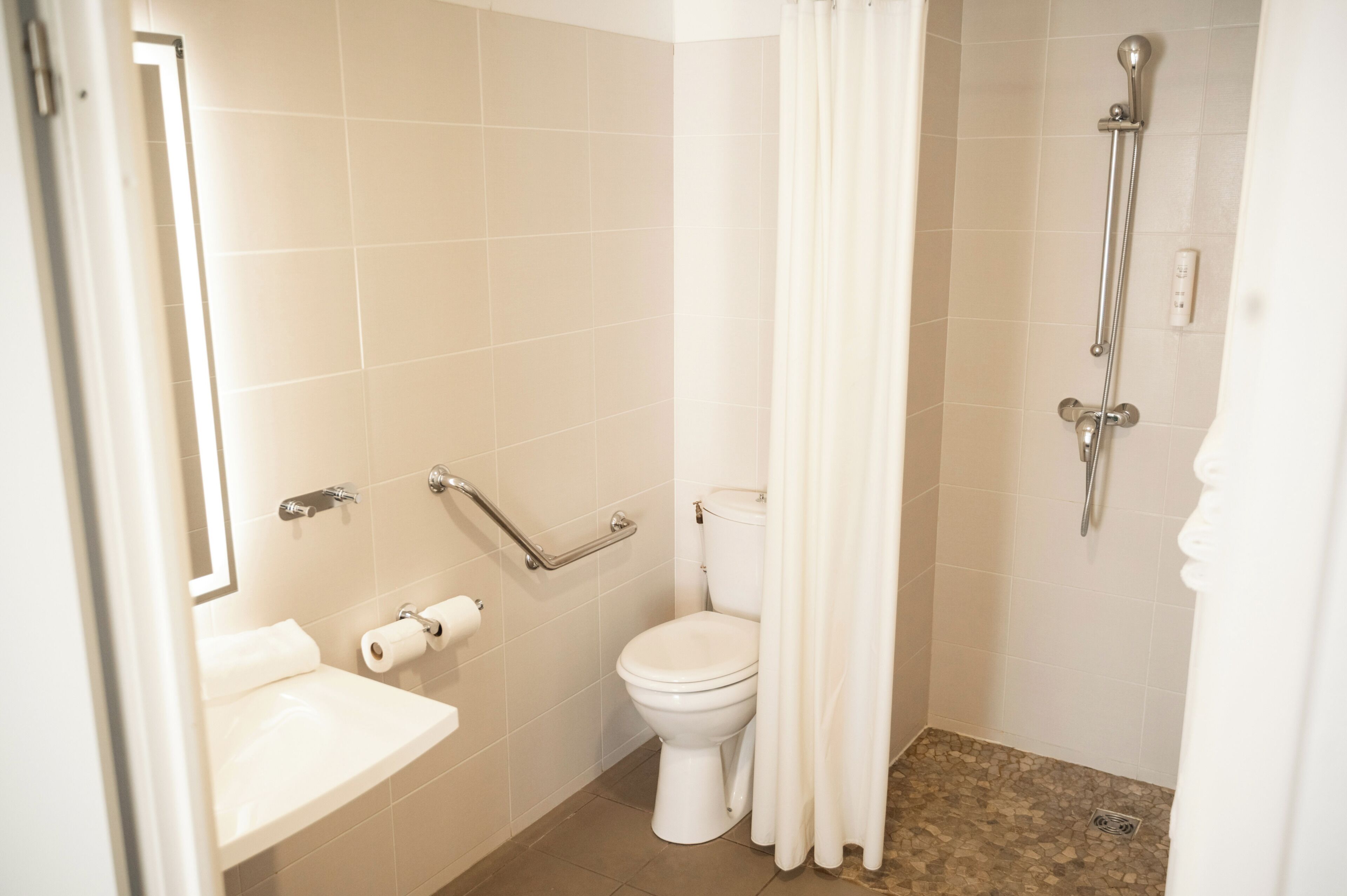 A bathroom with a toilet, a sink, a shower, and a grab bar.