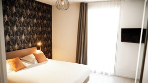 A hotel room with a large bed, a wall-mounted TV, and a patterned wallpaper. - Zenitude Hôtel - Résidences Narbonne Centre (Narbonne)