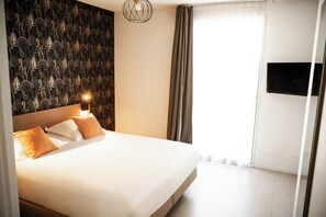 Habitación de hotel con una cama grande, un televisor de pared y un papel tapiz estampado.