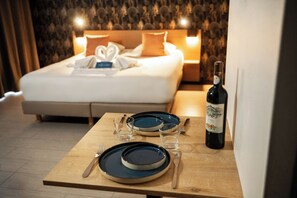 A neatly made bed with pillows, a bedside table with plates, cutlery, and a bottle of wine. - Zenitude Hôtel - Résidences Narbonne Centre (Narbonne)