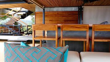 A modern outdoor seating area with wooden chairs and a sofa, a staircase, and a view of a mountainous landscape.