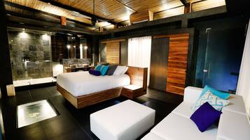 A modern bedroom with a bed, a sitting area, and a shower area.