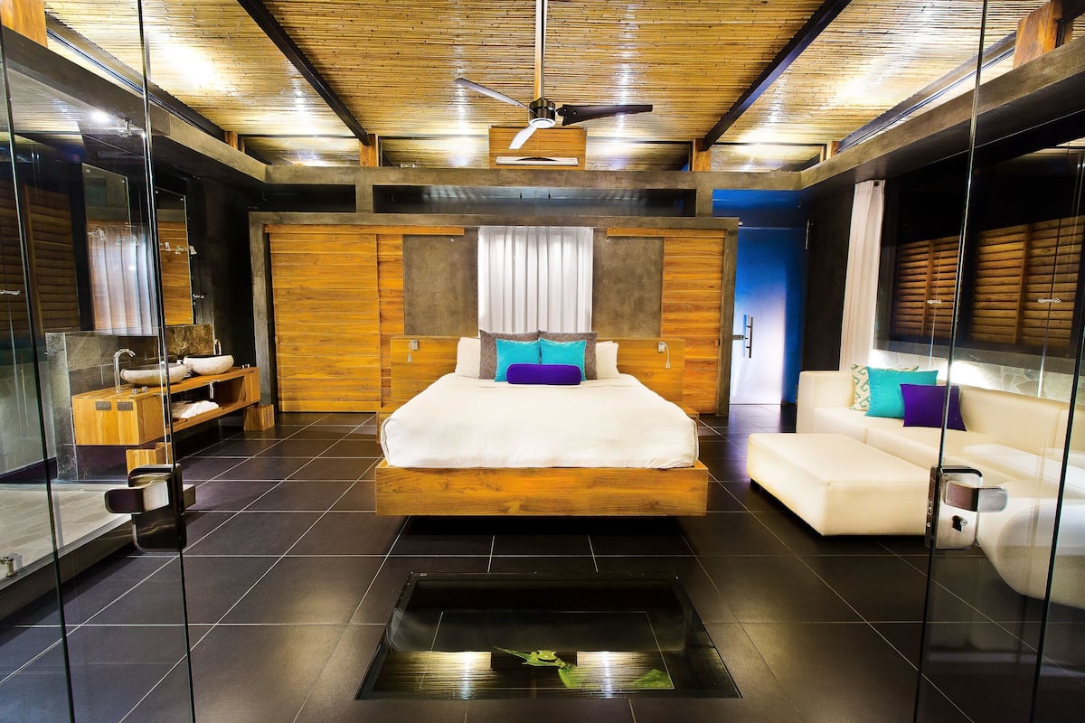 Un dormitorio moderno con cama, sofá, techo de madera y separador de vidrio.