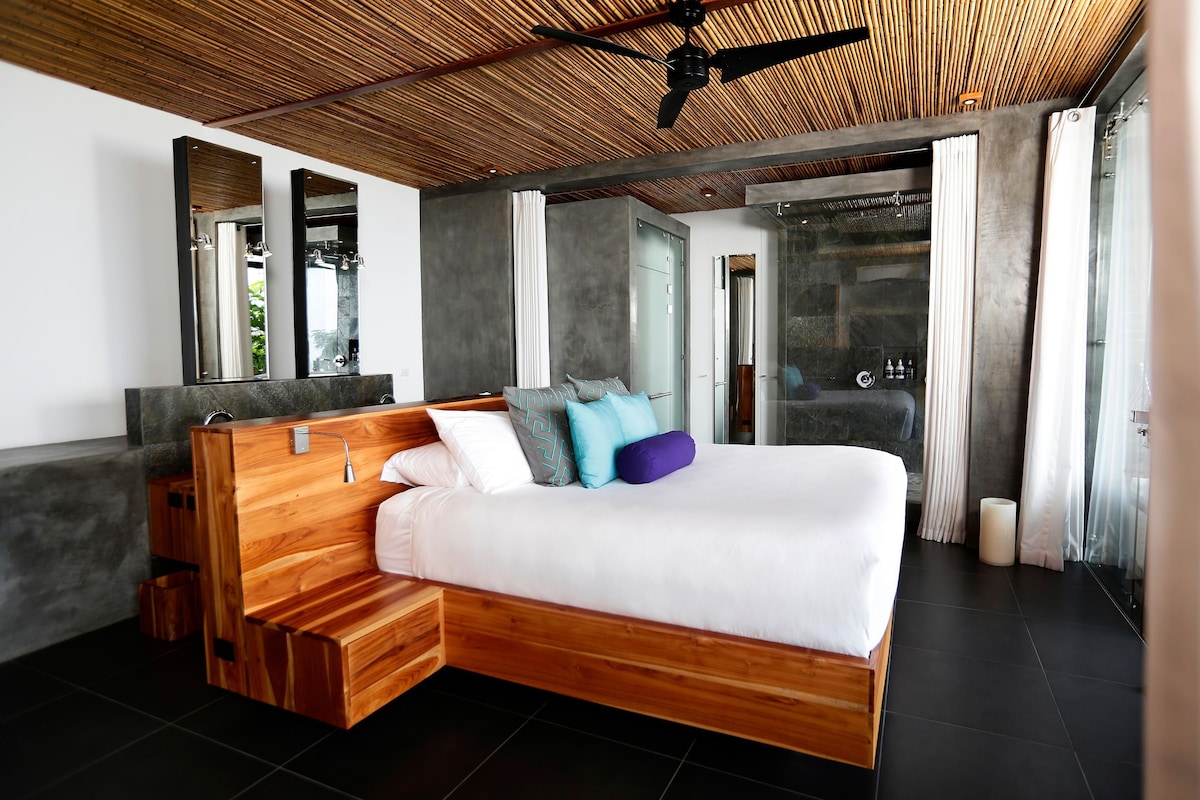 Un dormitorio moderno con una cama de madera, un banco empotrado y un espejo grande.