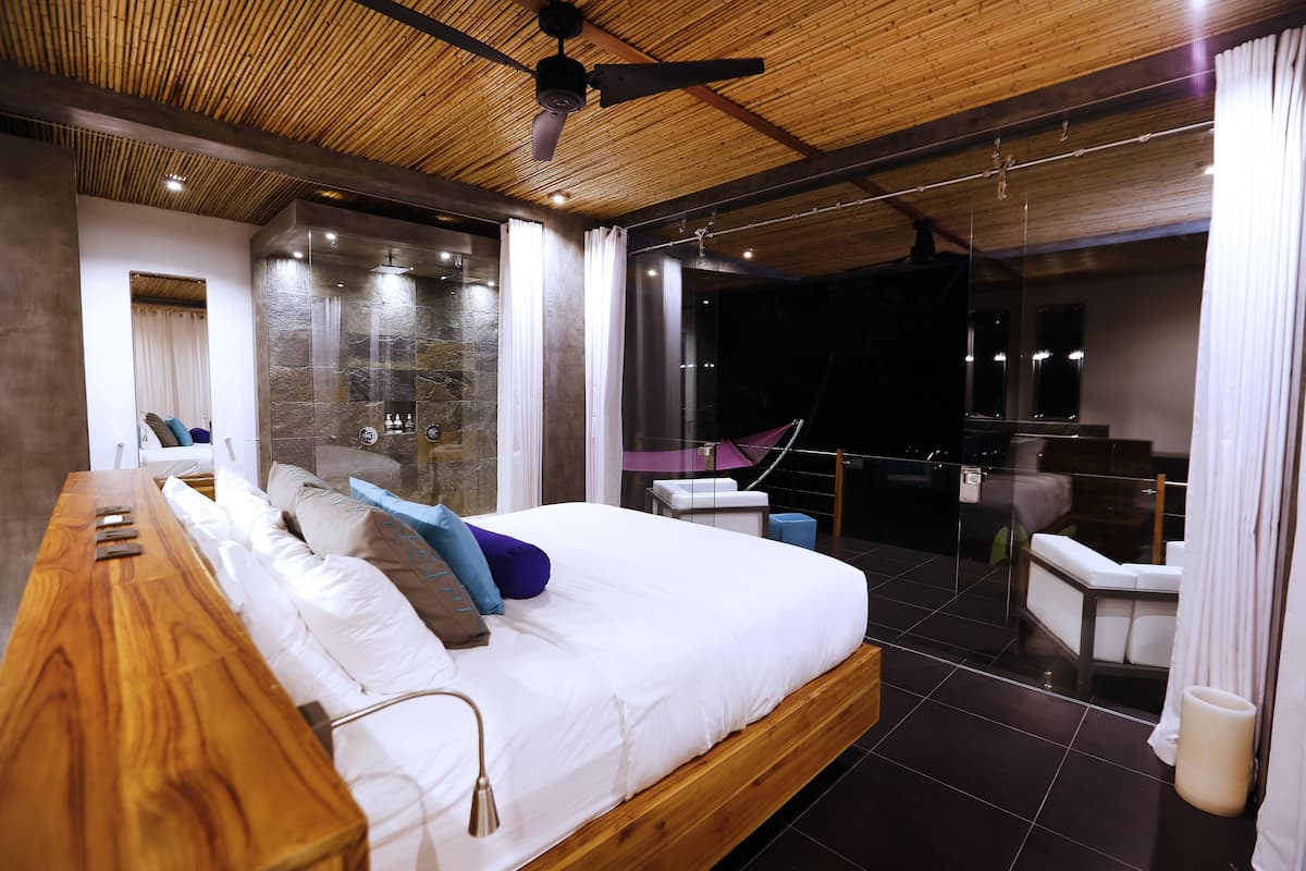 Un dormitorio moderno con una cama de madera, ducha de vidrio y balcón con vistas.