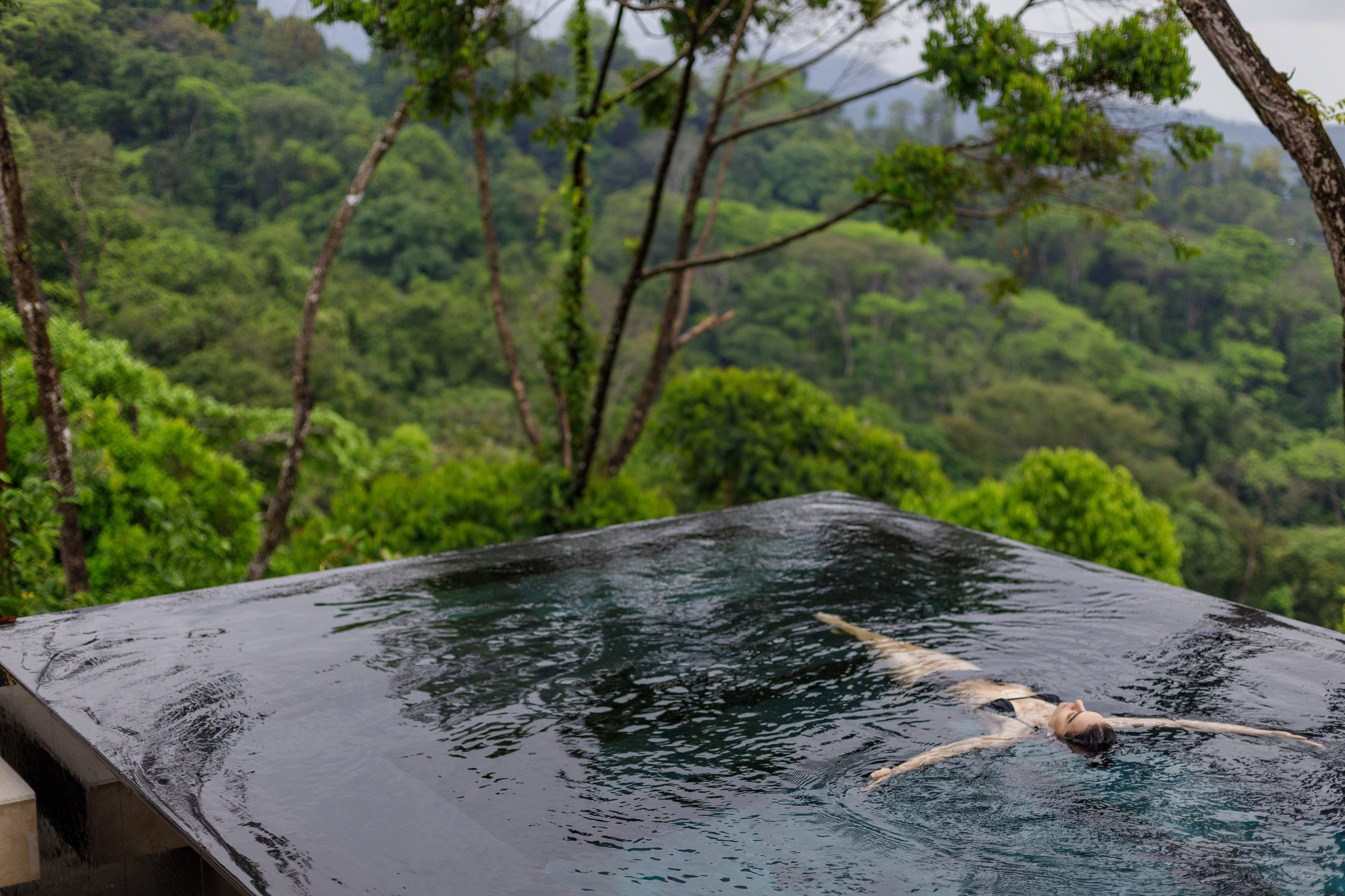 A person swimming in a hot tub with a lush forest view.