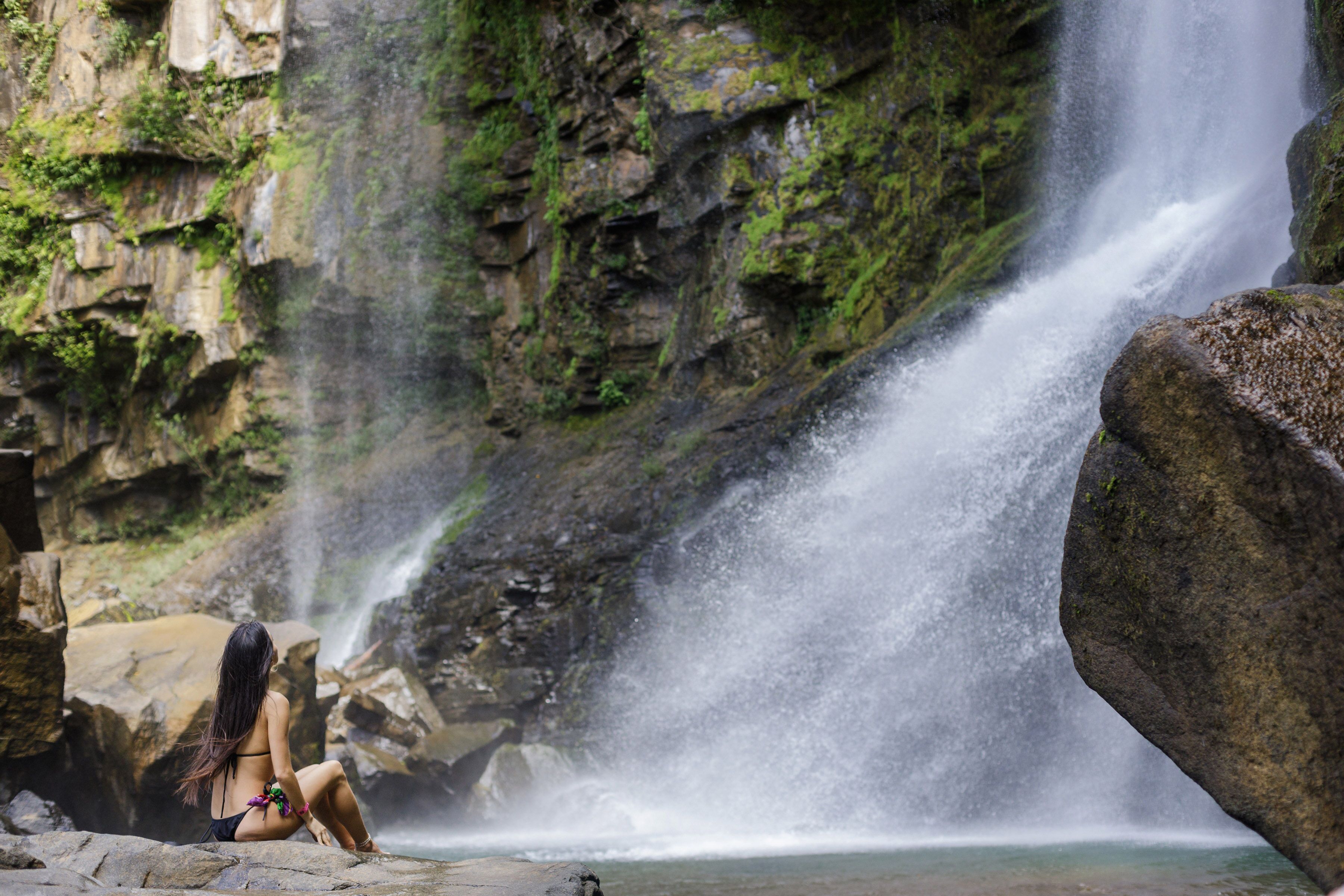 Una donna seduta vicino a una cascata in un ambiente naturale.