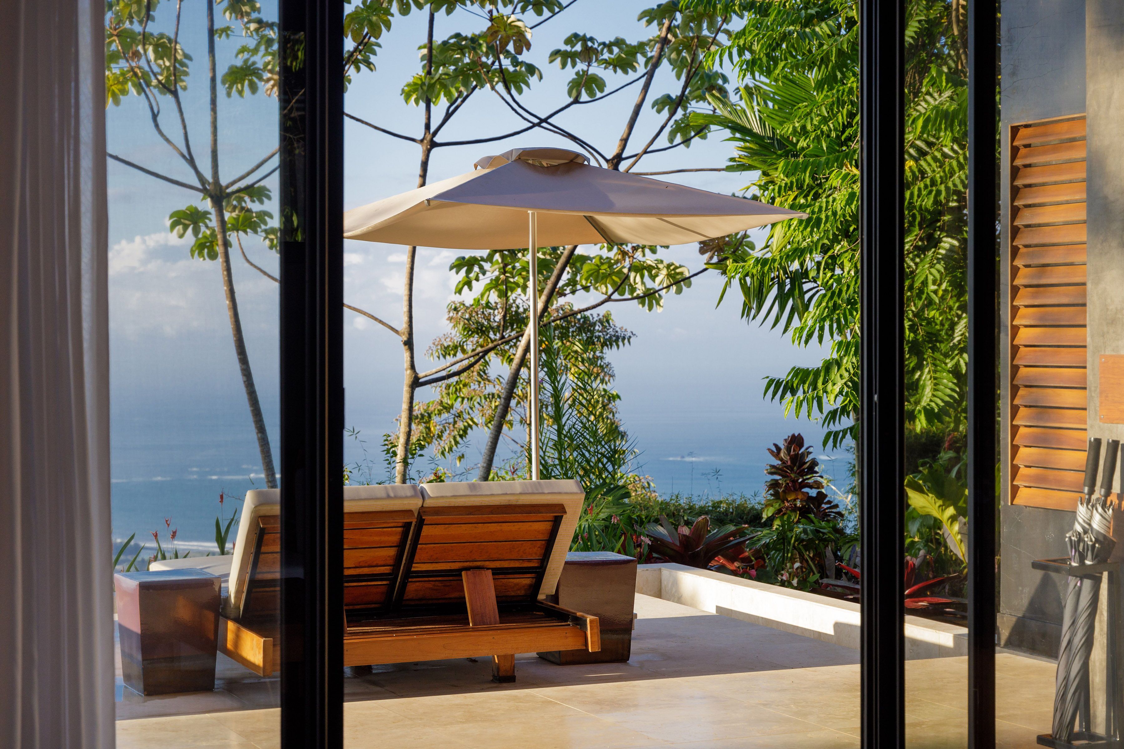 A modern outdoor seating area with a wooden bench and a large umbrella, overlooking a scenic ocean view.